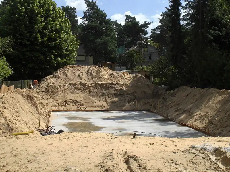 Dalle de béton fraîchement coulée avec coffrage métallique au fond d'une fouille sableuse, grands tas de sable autour