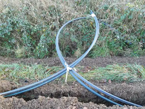 Quatre tuyaux noirs à liserés bleu et vert attachés ensemble, posés au-dessus d'une tranchée étroite dans un talus herbeux